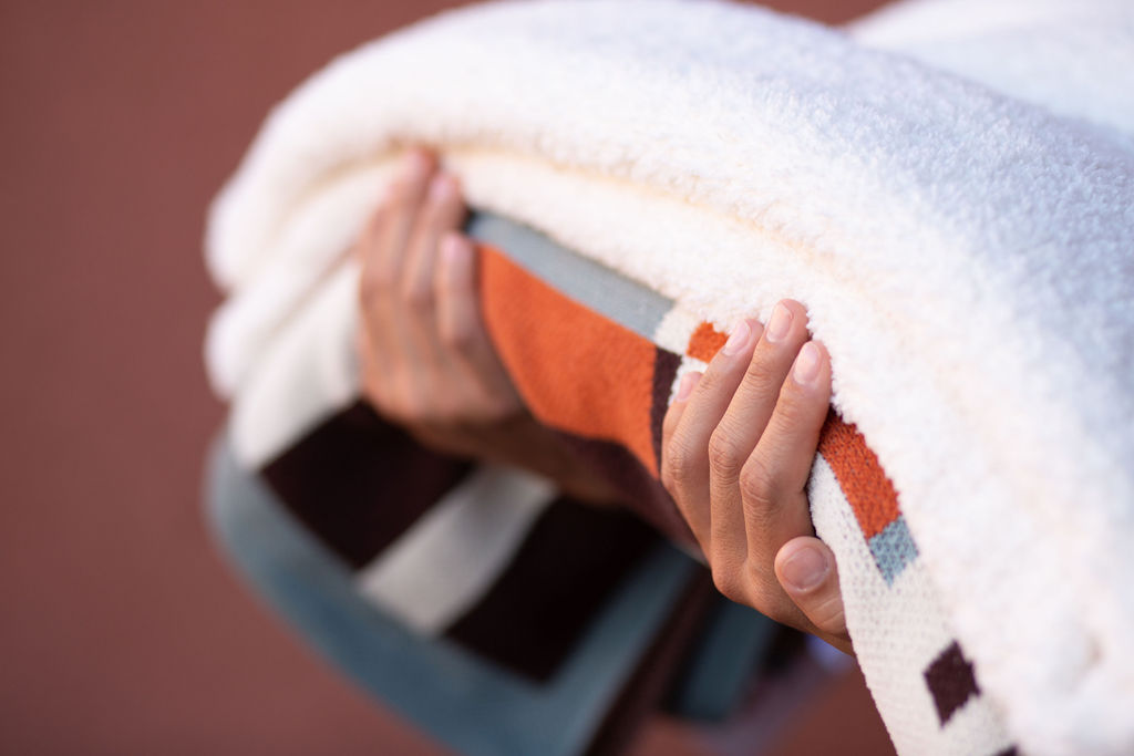 two hands holding white blanket and multi colored blanket