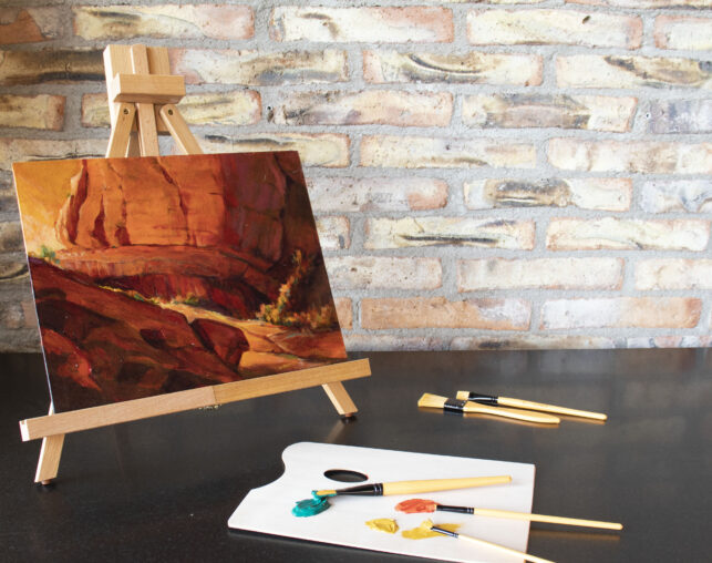 red rock acrylic painting on small wooden easel with paint and brushes next to it