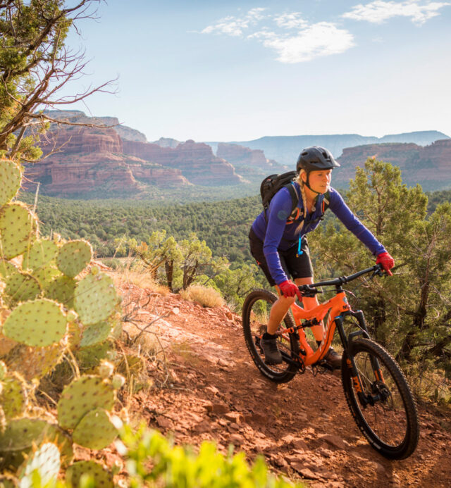 Woman on orange mountain bike with cactus on trail