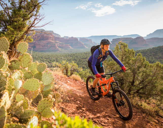 Woman on orange mountain bike with cactus on trail