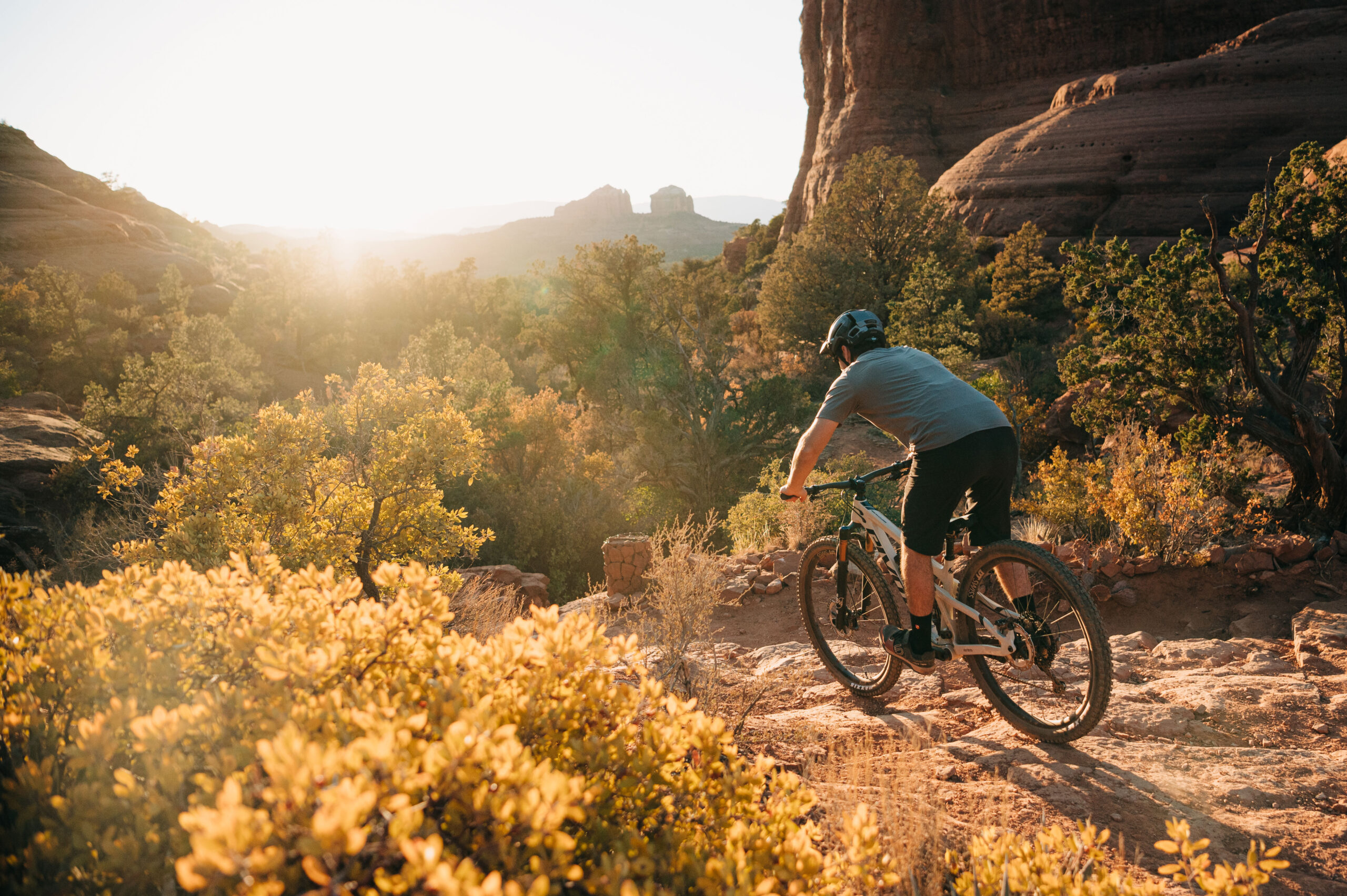 man in gray shirt riding mountain bike into the sunset