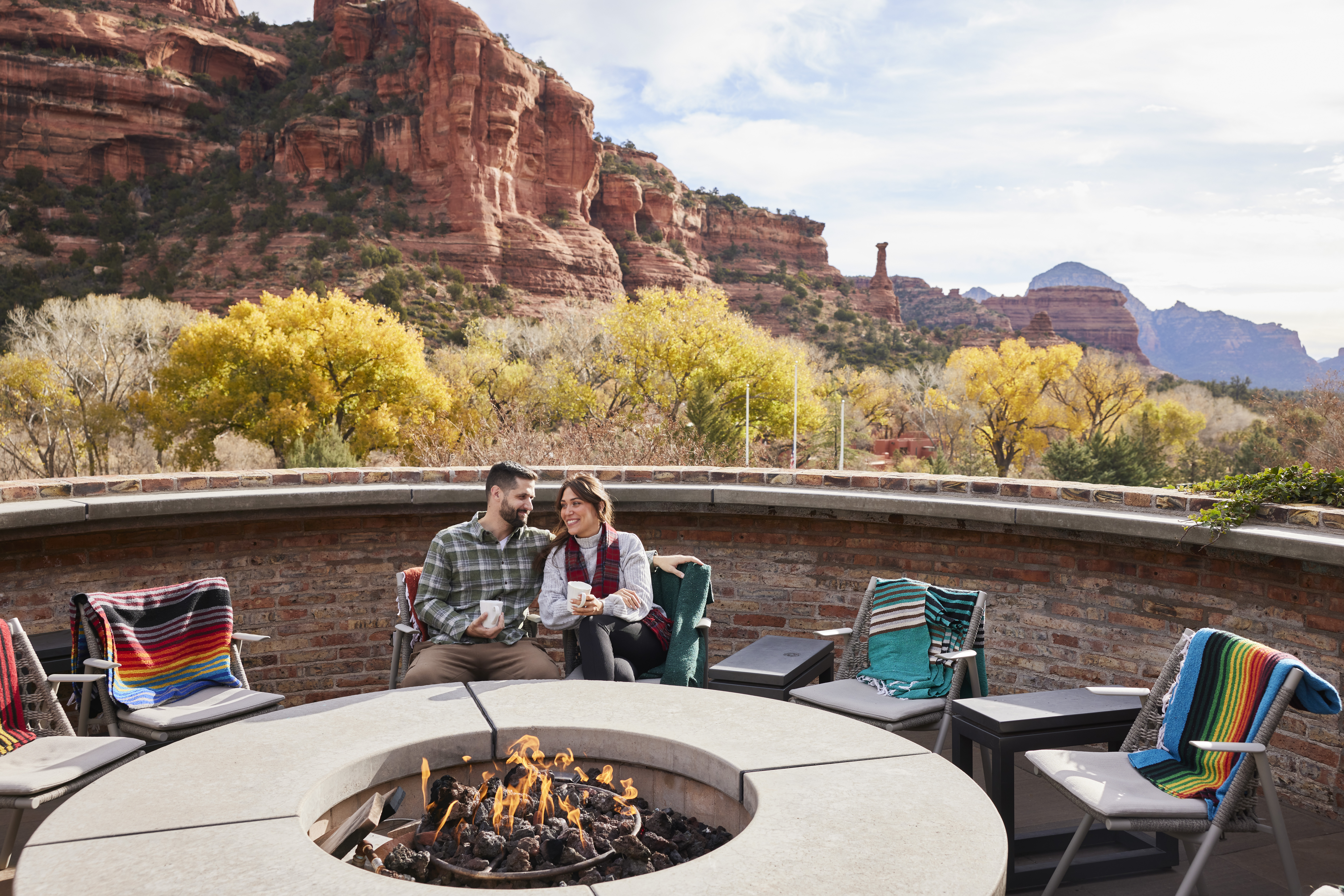 two guests sitting at firepit with red rock views in background