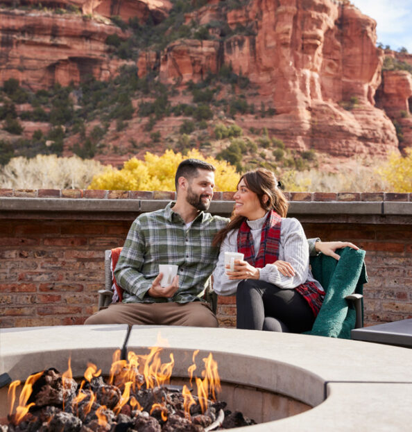 two guests sitting at firepit with red rock views in background